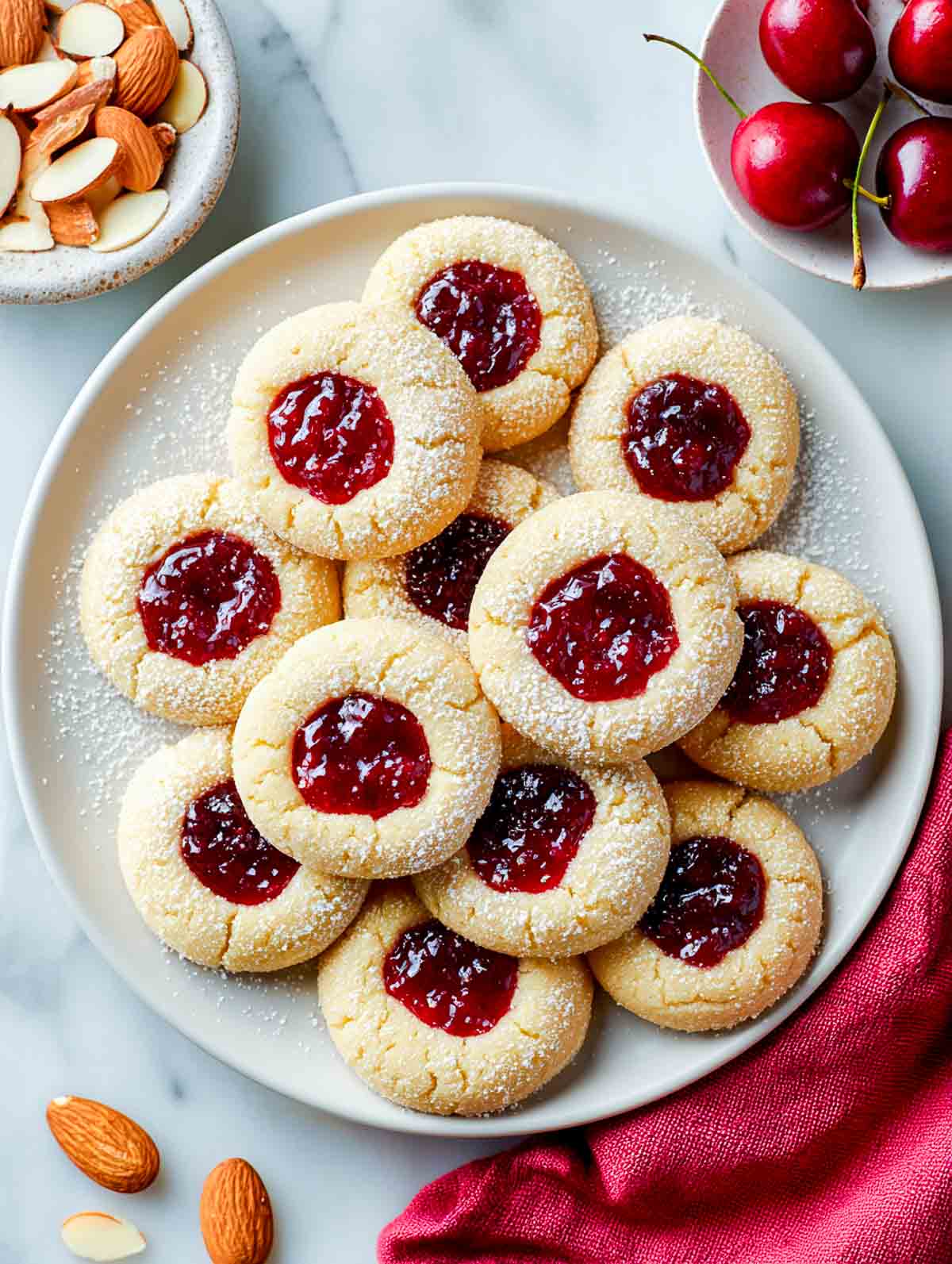 Cherry almond thumbprint cookies filled with red jam on a white plate.