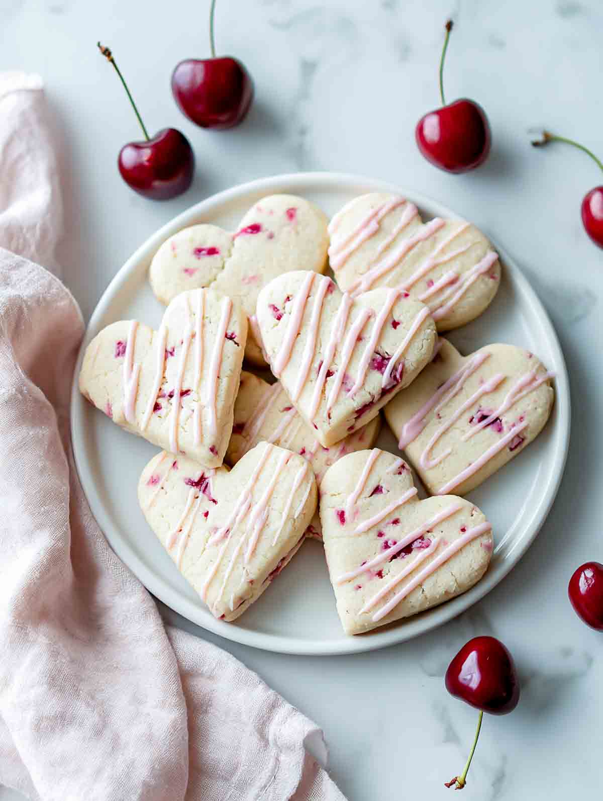 Cherry vanilla heart cookies with pink drizzle on a white plate.