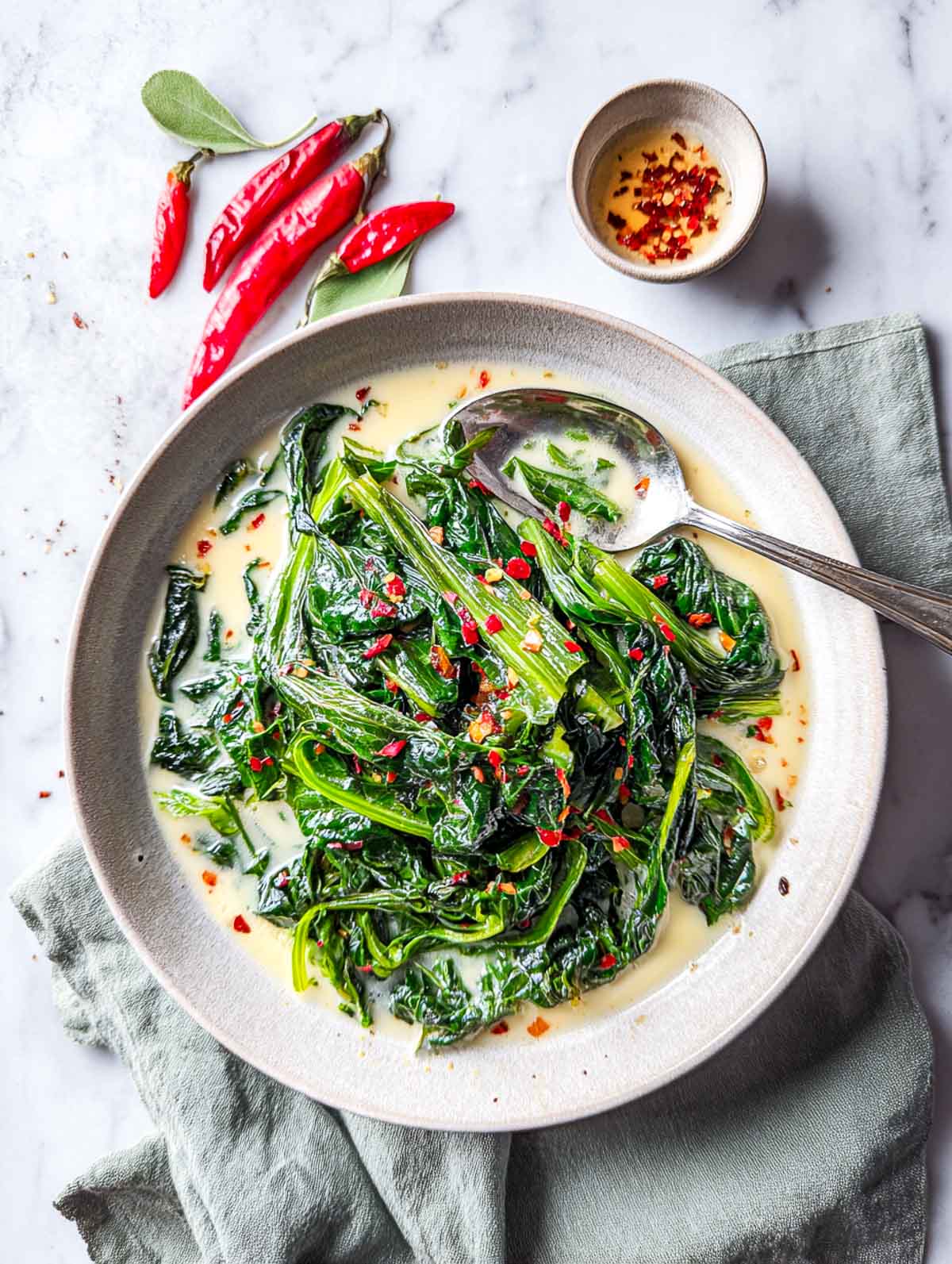 A bowl of tender spring greens braised in coconut milk and topped with garlic chili oil and red pepper flakes.