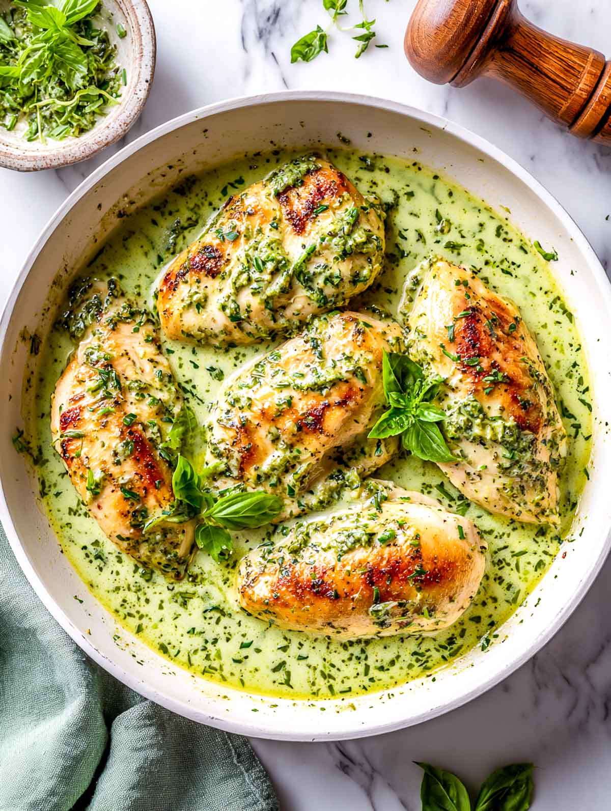 Golden chicken breasts simmered in a creamy green herb sauce in a skillet.