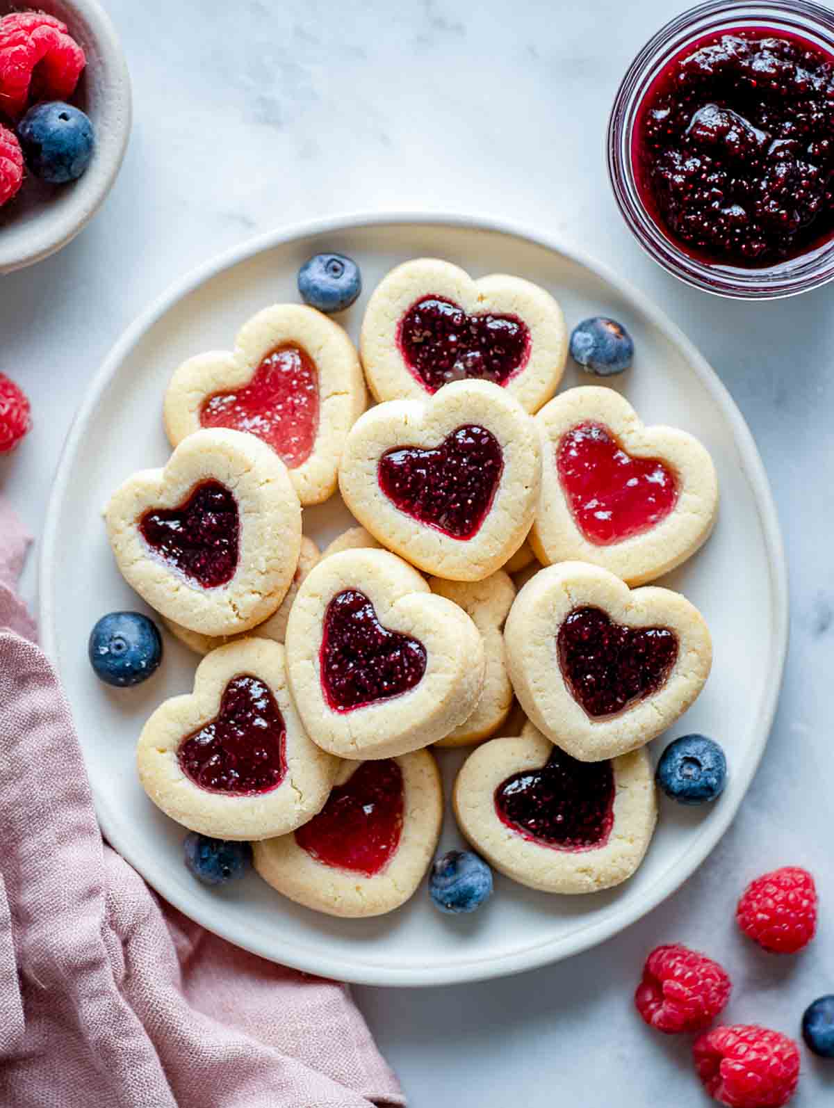 Heart-shaped jam drop cookies filled with mixed berry jam on white plate.