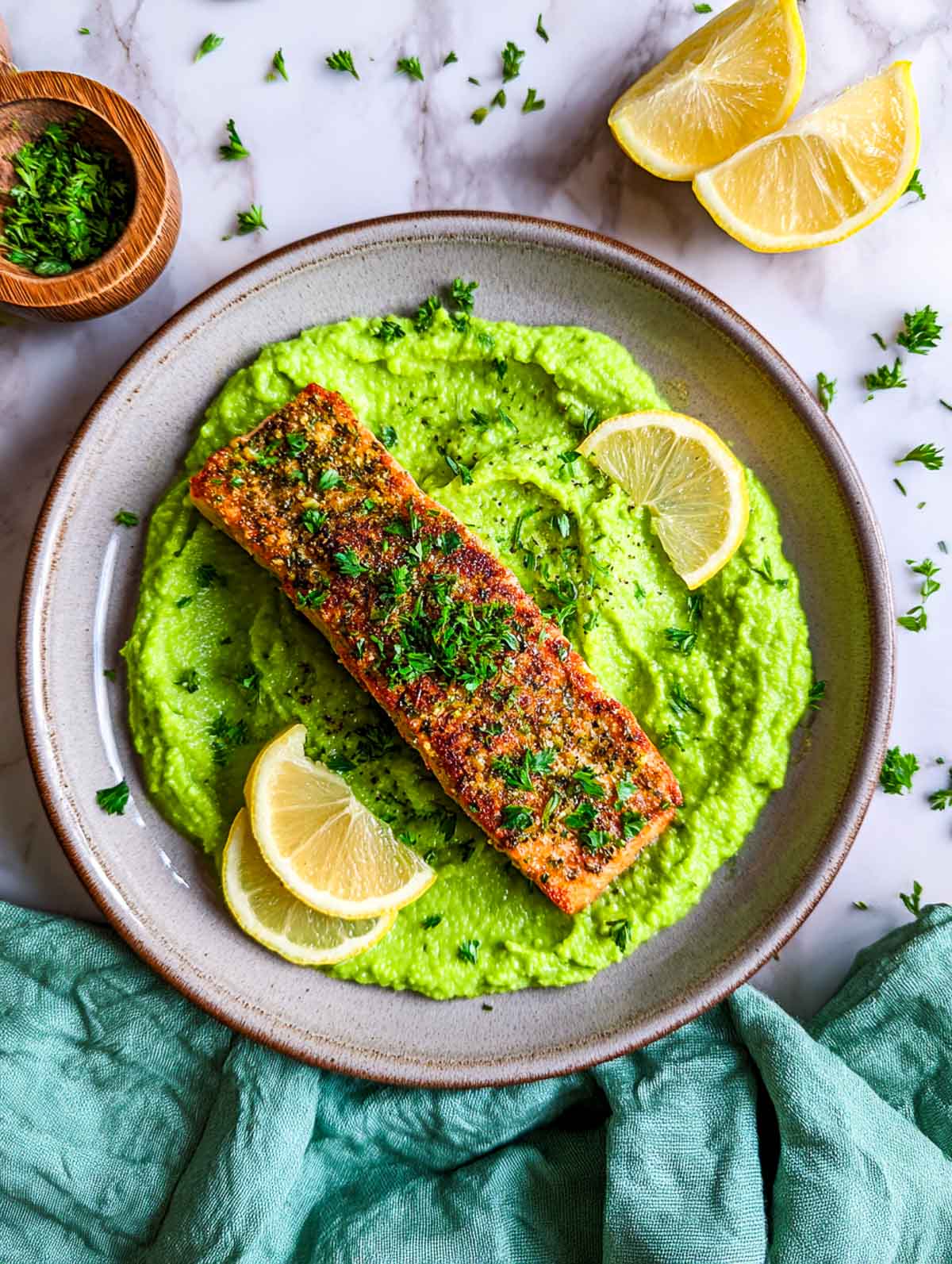 Herb-crusted salmon served over bright green pea purée with lemon wedges.