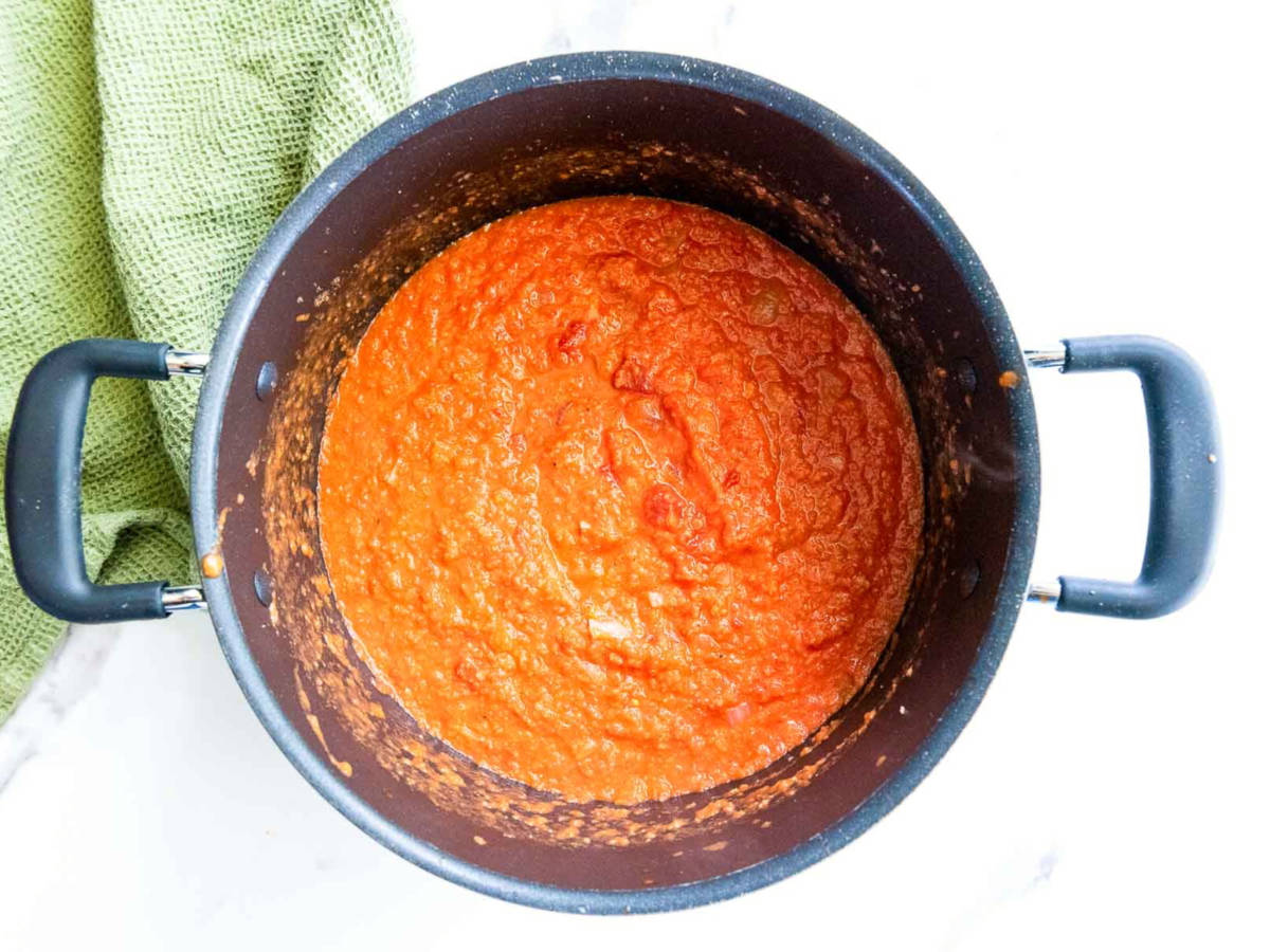Thick tomato sauce simmering in a large pot, cooked down to a rich, deep red base for jollof rice.