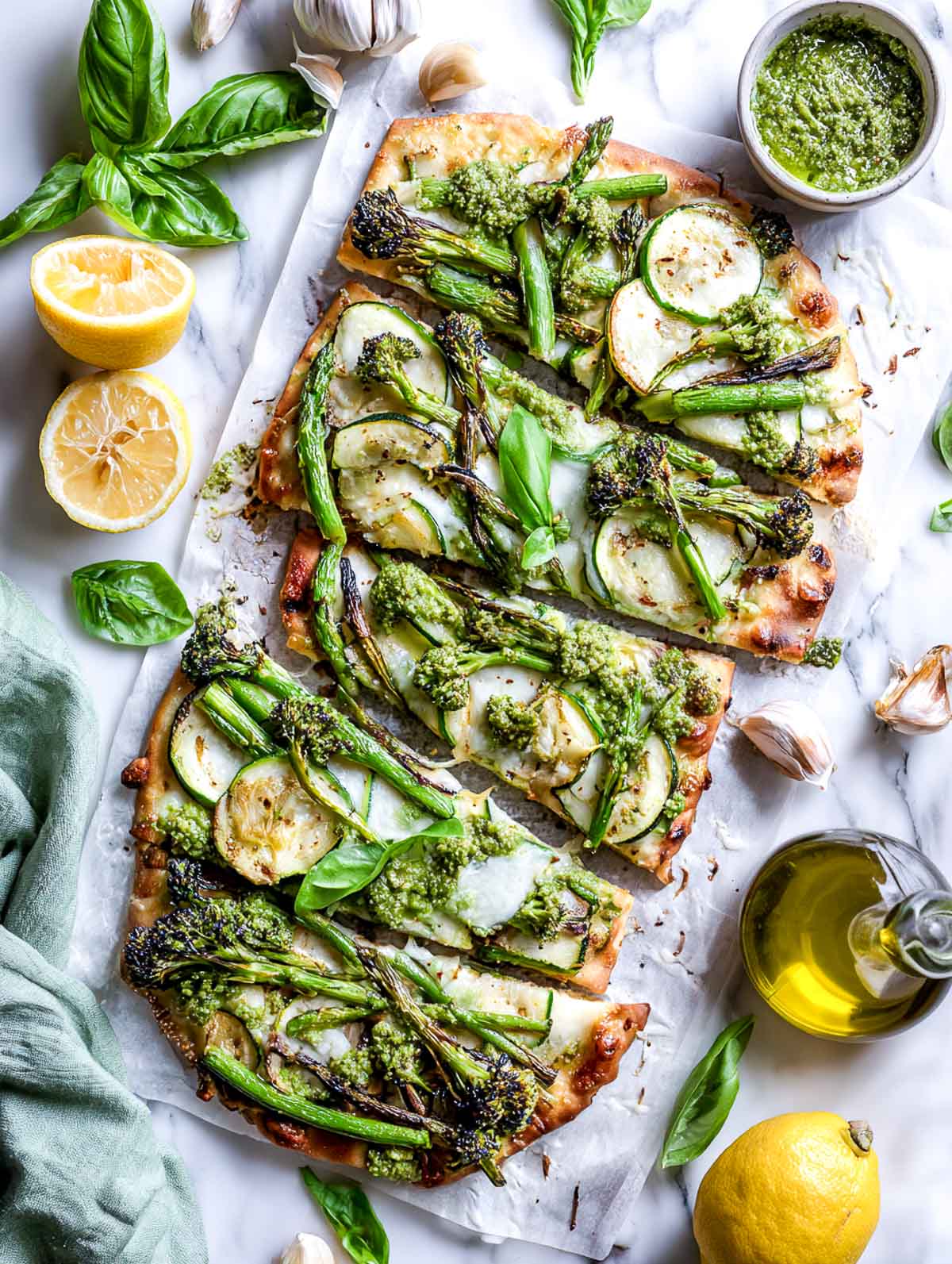 Sliced pesto flatbread topped with roasted green vegetables and melted cheese.