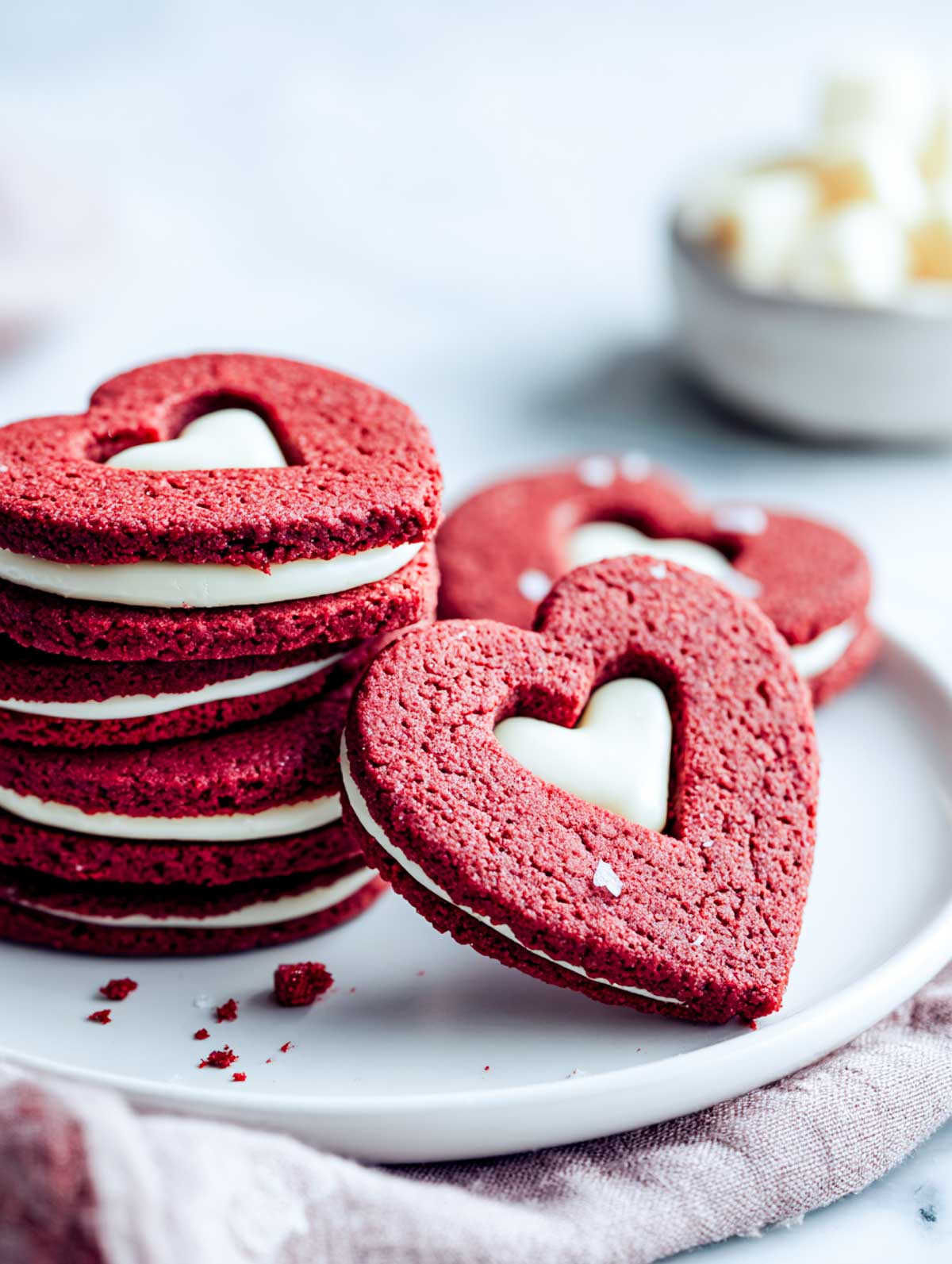 Red velvet linzer cookies with heart cutouts and white chocolate filling on a plate.
