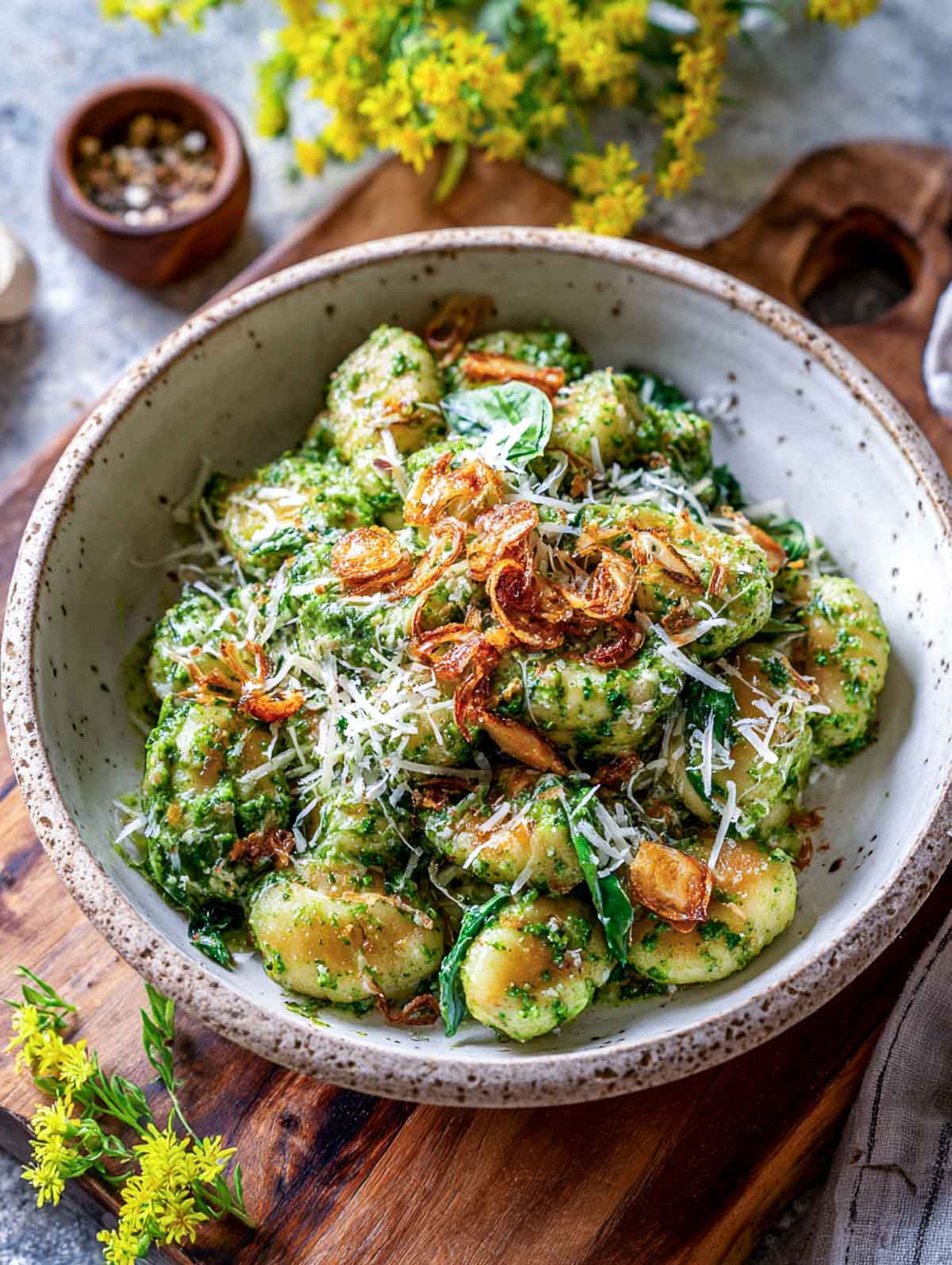A bowl of creamy spinach pesto gnocchi topped with crispy garlic slices.