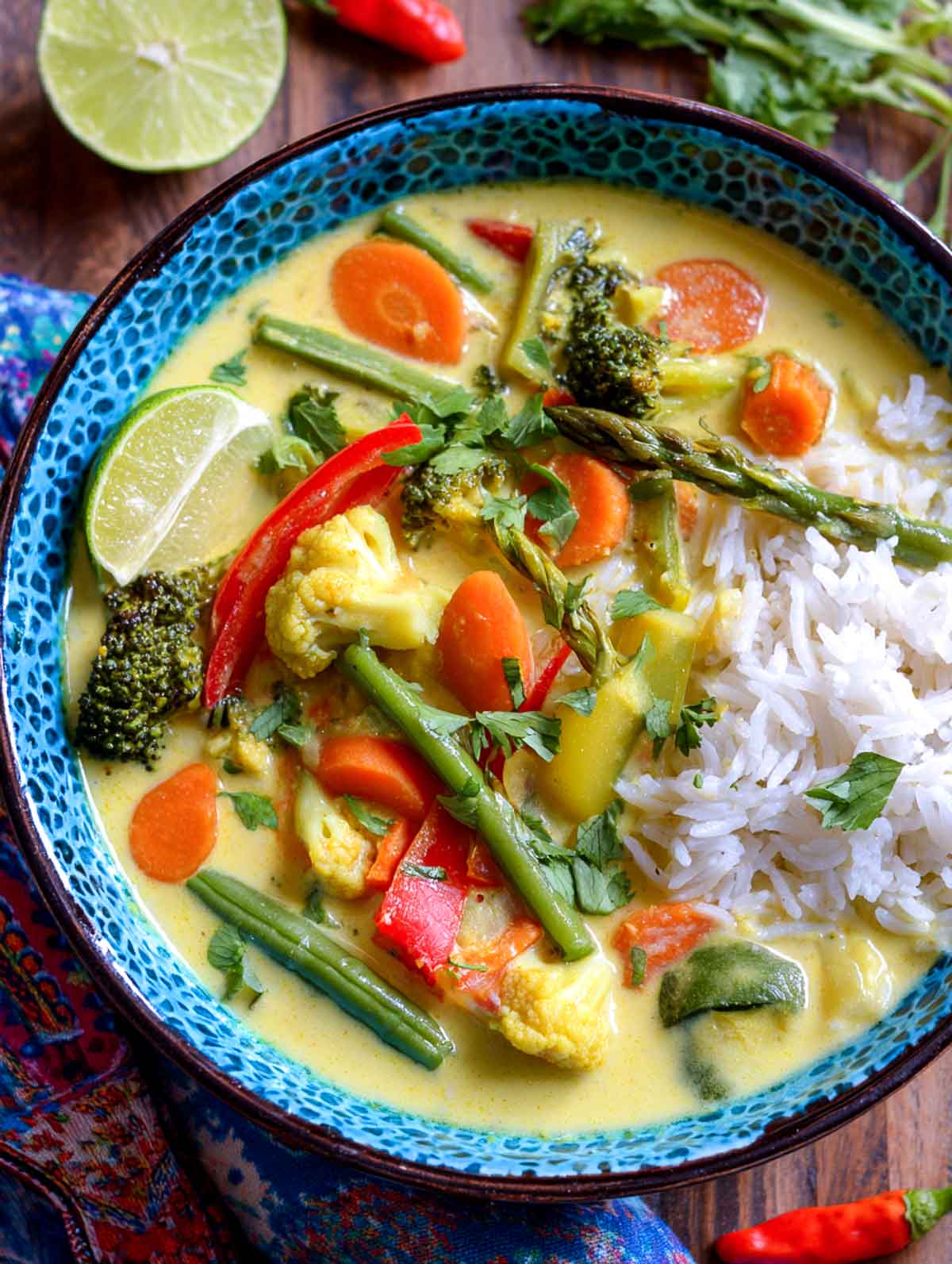 Vegan spring vegetable coconut curry with rice and fresh lime served in a blue bowl.