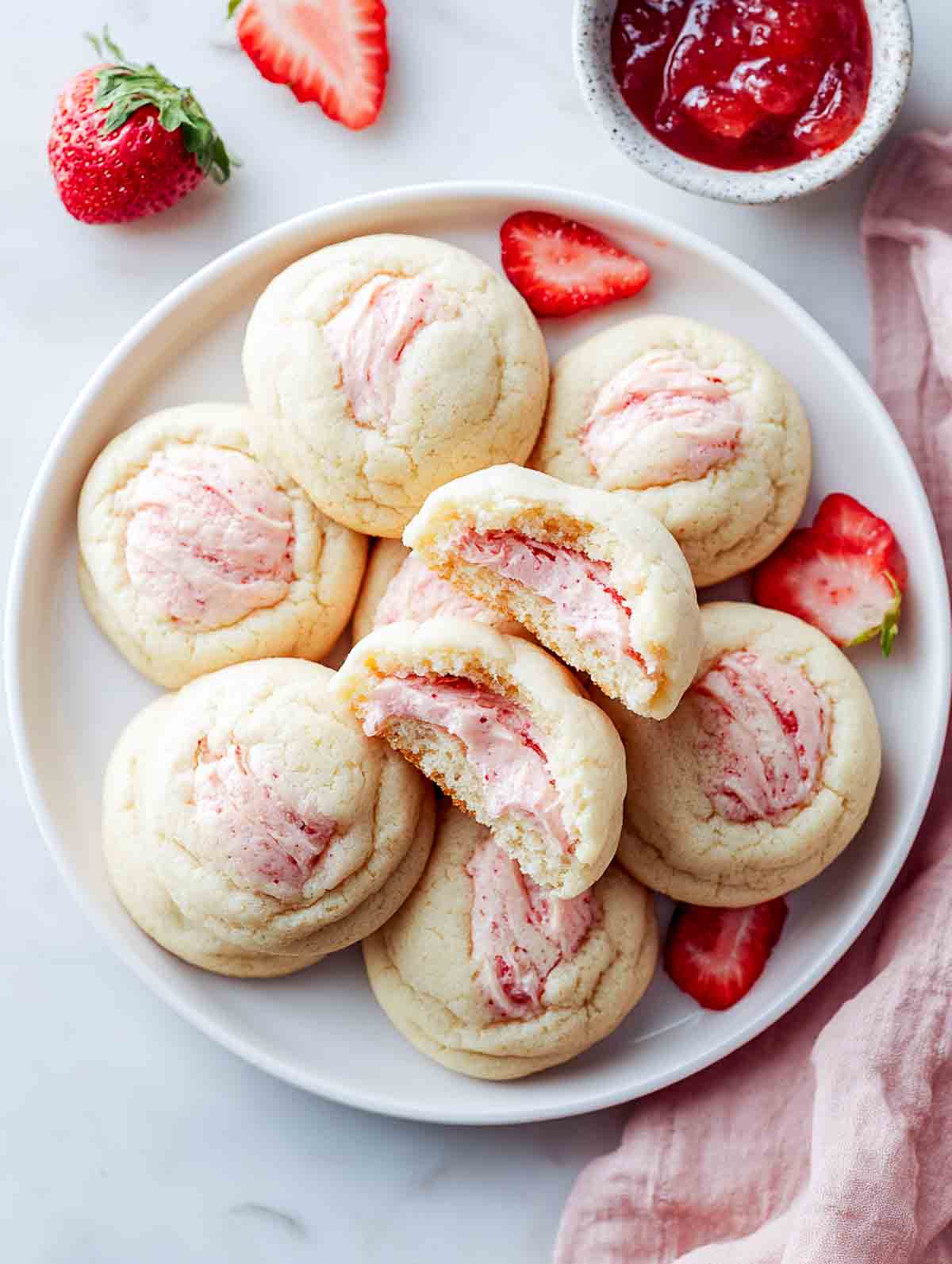 Strawberry cheesecake stuffed sugar cookies on a plate with one cookie broken open.