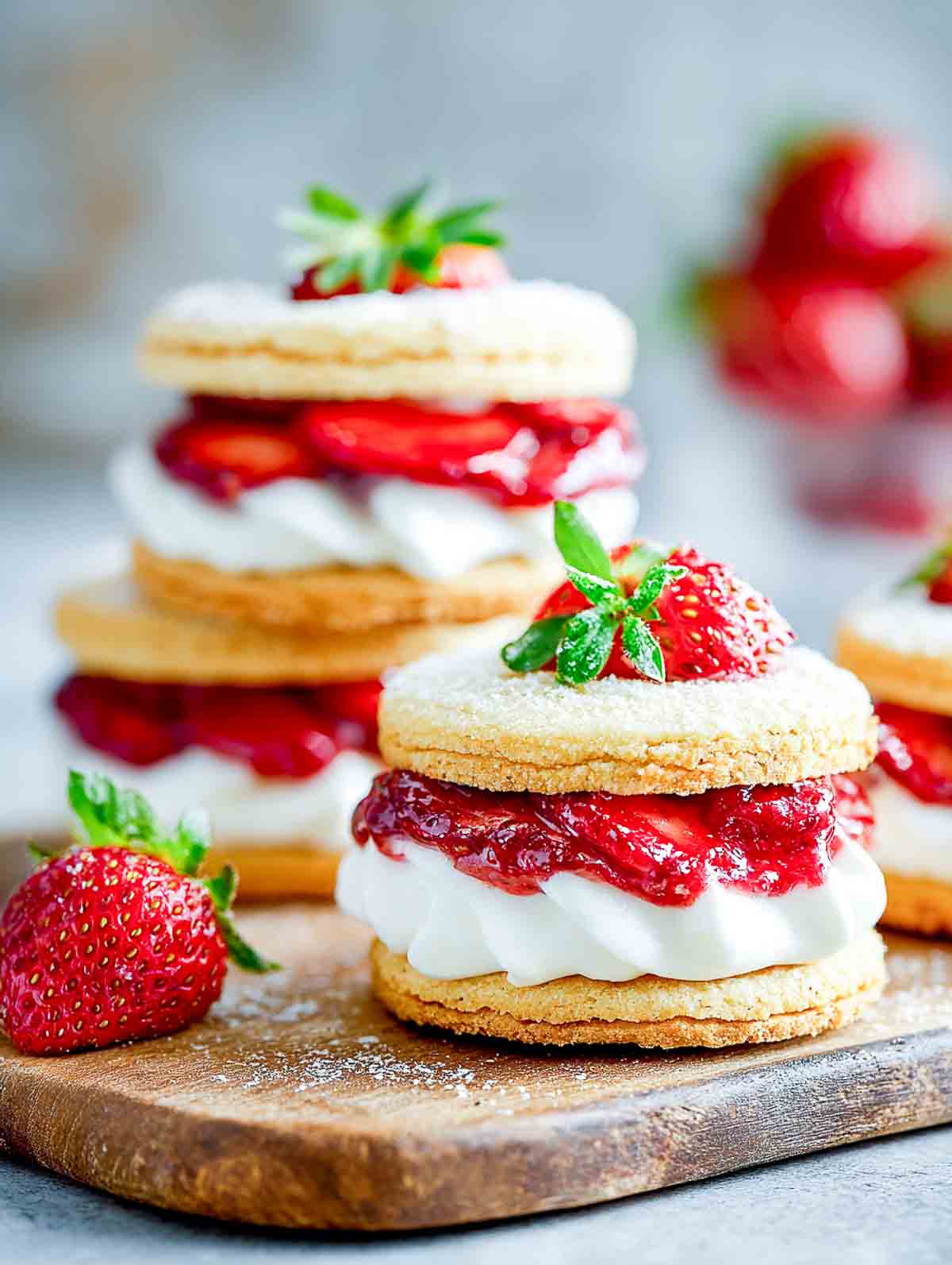 Strawberry shortcake sandwich cookies with cream and strawberry jam on a white plate.