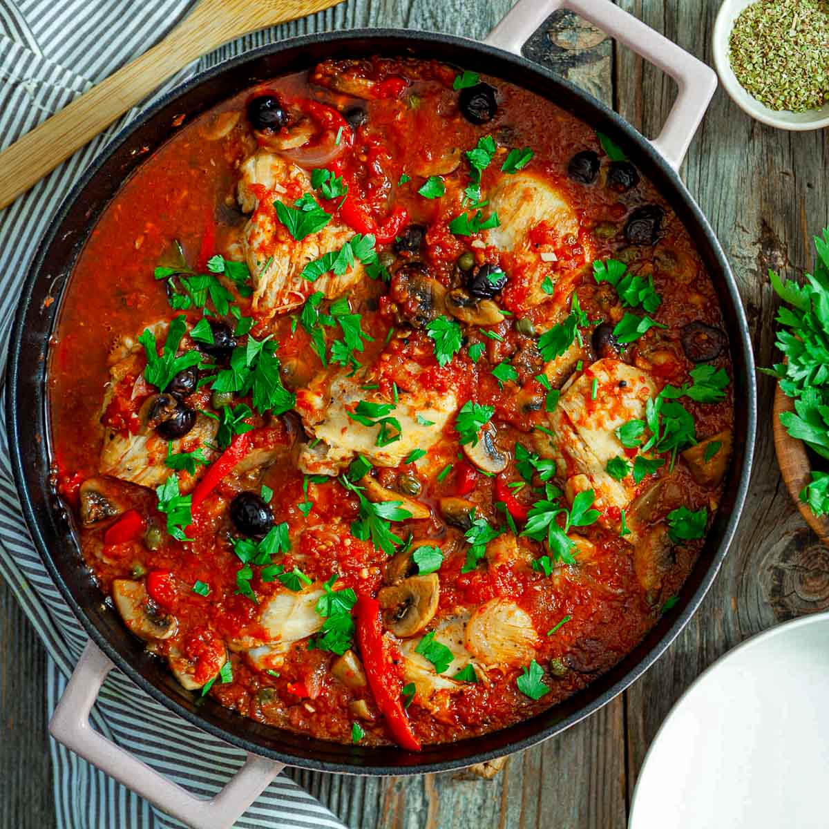 Overhead view of classic chicken cacciatore in a pan with tender chicken pieces in tomato sauce, topped with parsley and olives.