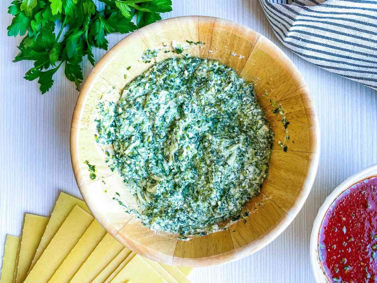 Spinach ricotta filling in a bowl with lasagna noodles and marinara sauce nearby