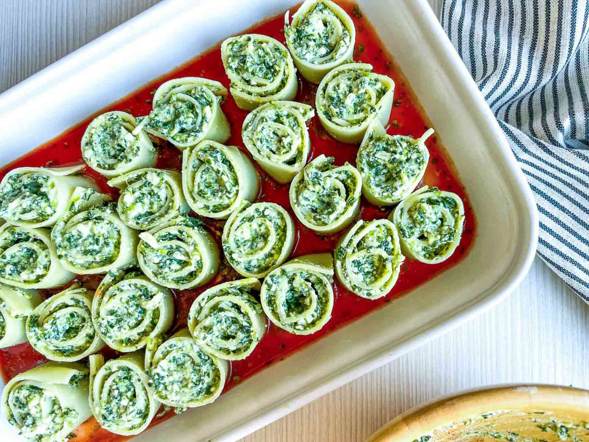 Spinach ricotta lasagna roll-ups arranged in a baking dish with marinara sauce