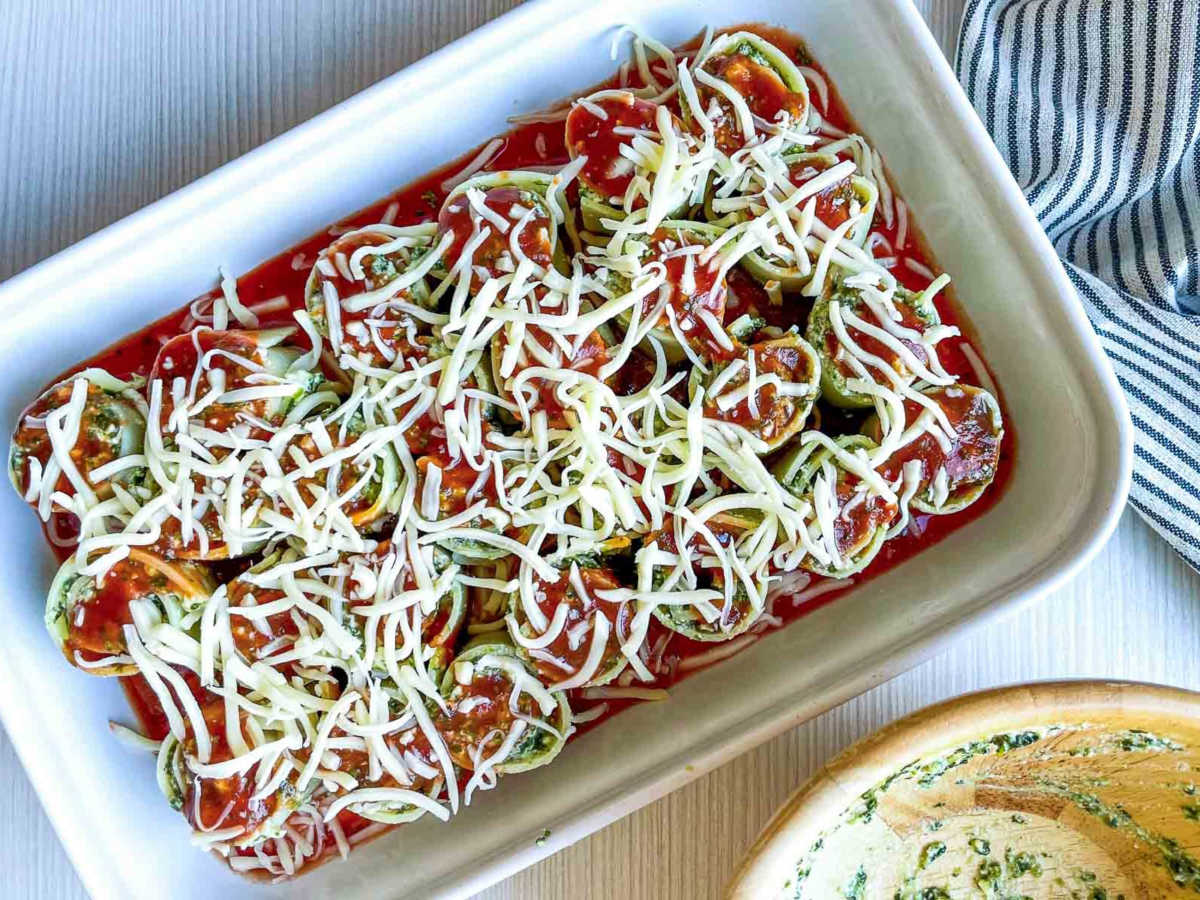 Spinach ricotta lasagna roll-ups topped with marinara sauce and shredded mozzarella before baking