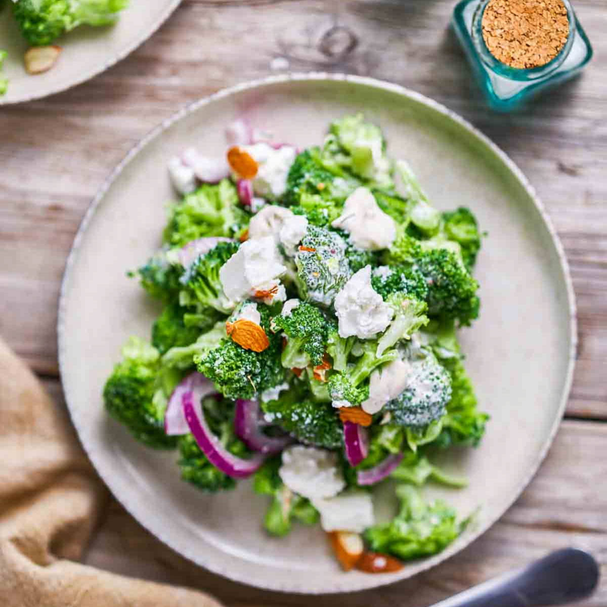 Close up of broccoli salad with feta, red onion, and sliced almonds on a plate.