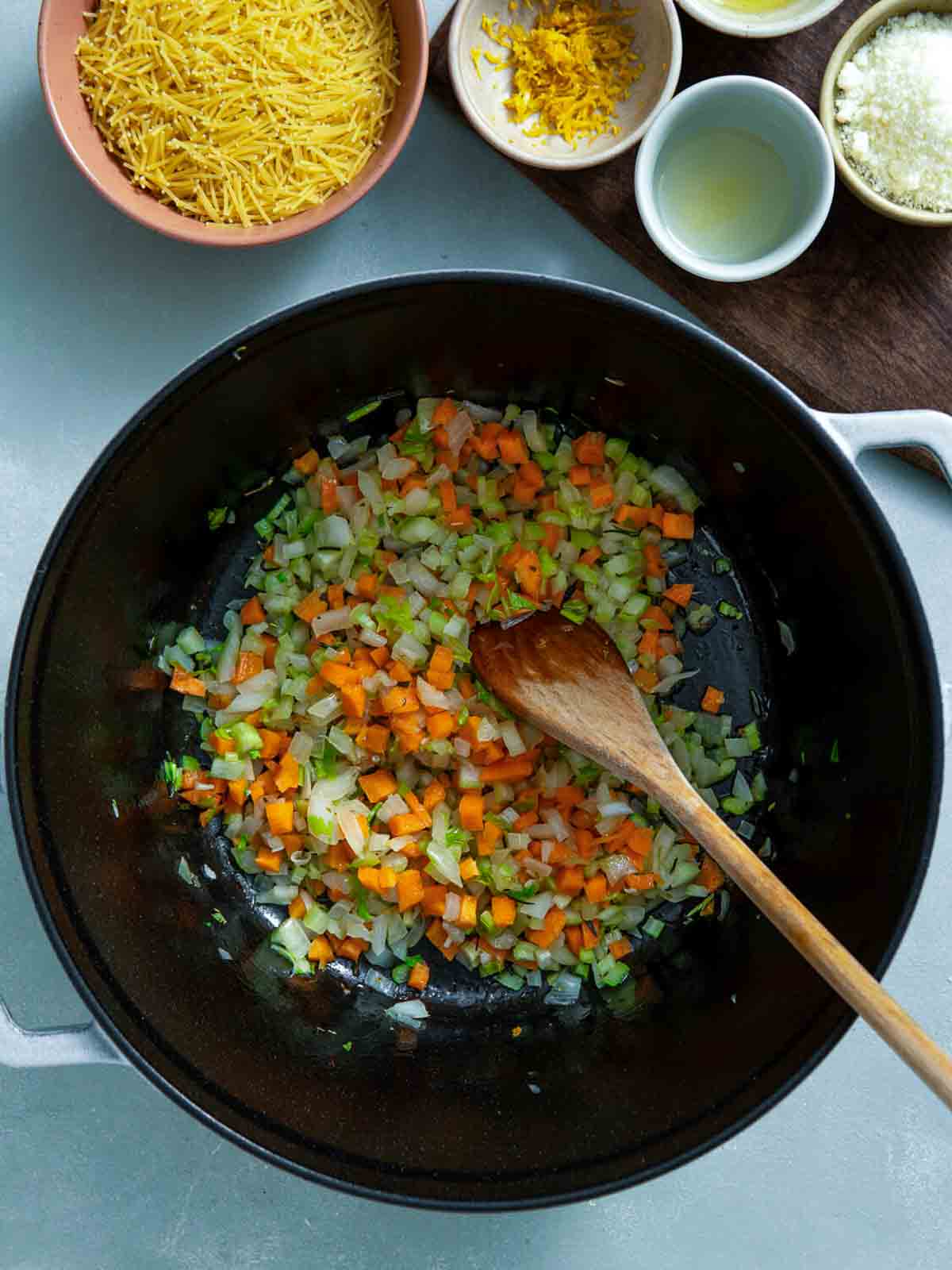 Diced onions, carrots, and celery sautéing in a pot with a wooden spoon.