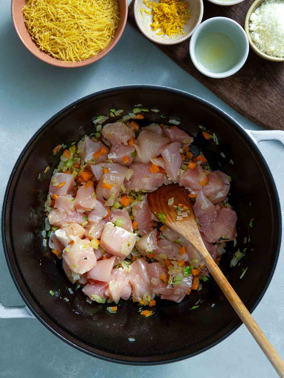 Diced chicken added to sautéed onions, carrots, and celery in a pot.