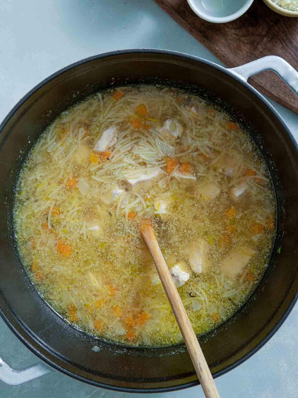 Fideo noodles cooking in chicken broth with diced vegetables and chicken.