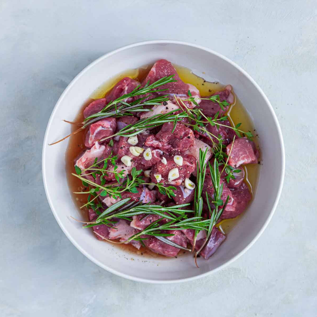 Raw marinated meat with herbs and garlic in bowl