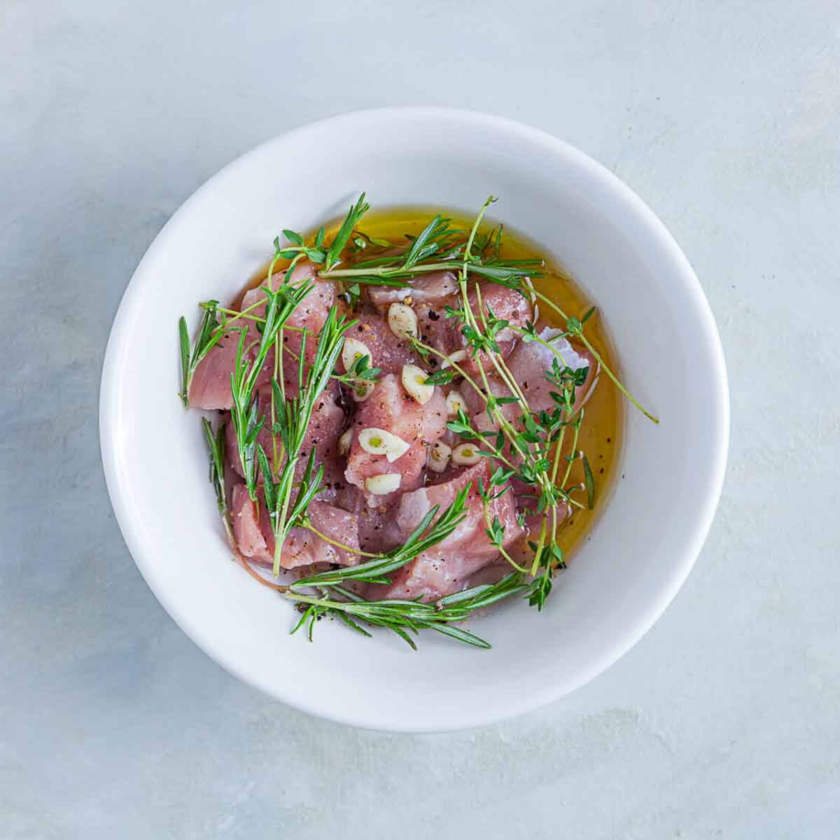 Raw meat marinating with olive oil, garlic slices, and fresh herbs like rosemary and thyme