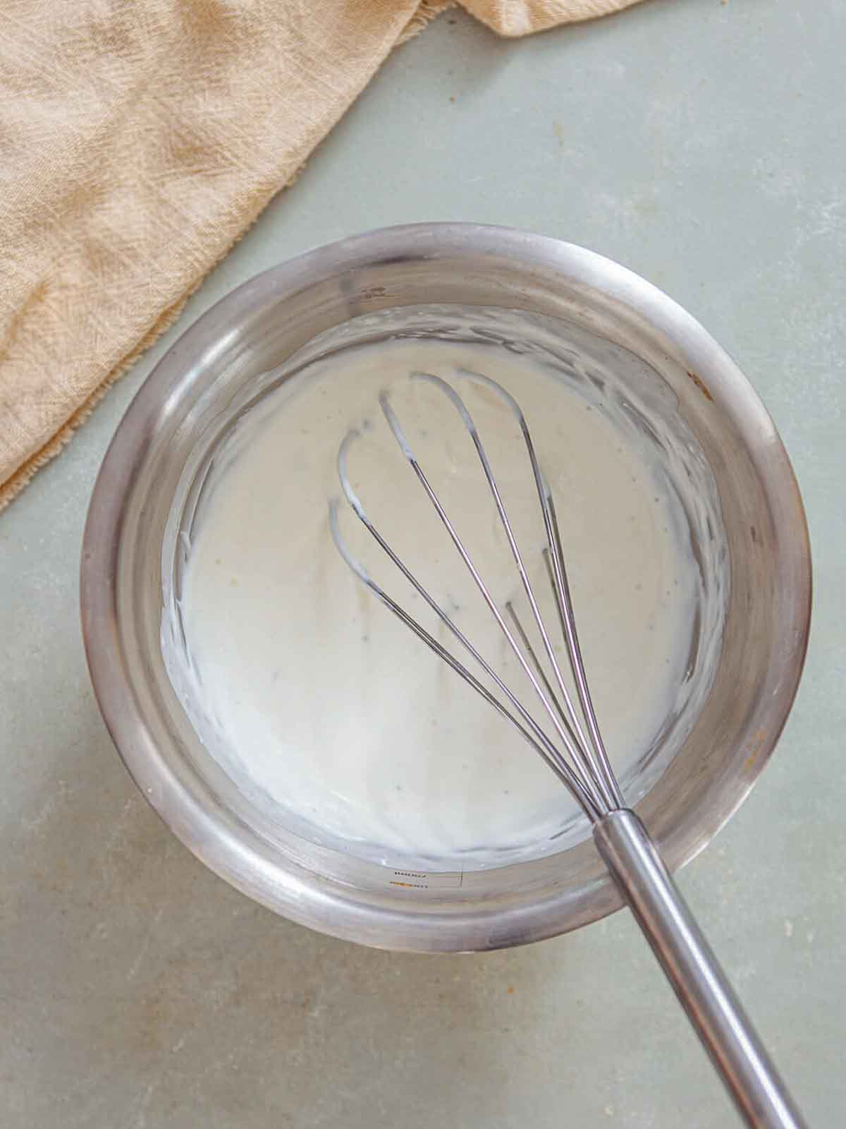 A metal mixing bowl with a whisk stirring a smooth, creamy mixture-likely cream being incorporated to finish the soup's silky texture