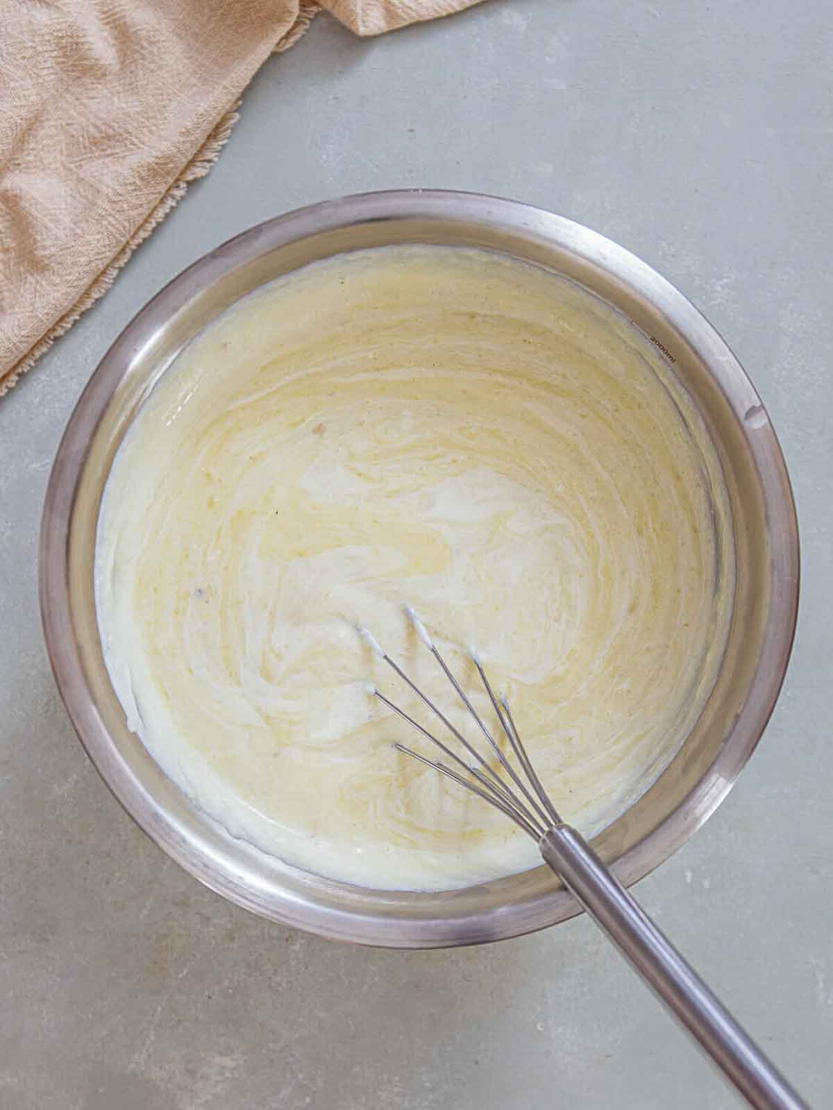 A mixing bowl with a whisk blending the potato-leek puree and cream together-now forming a smooth, pale, velvety soup mixture ready to chill or serve