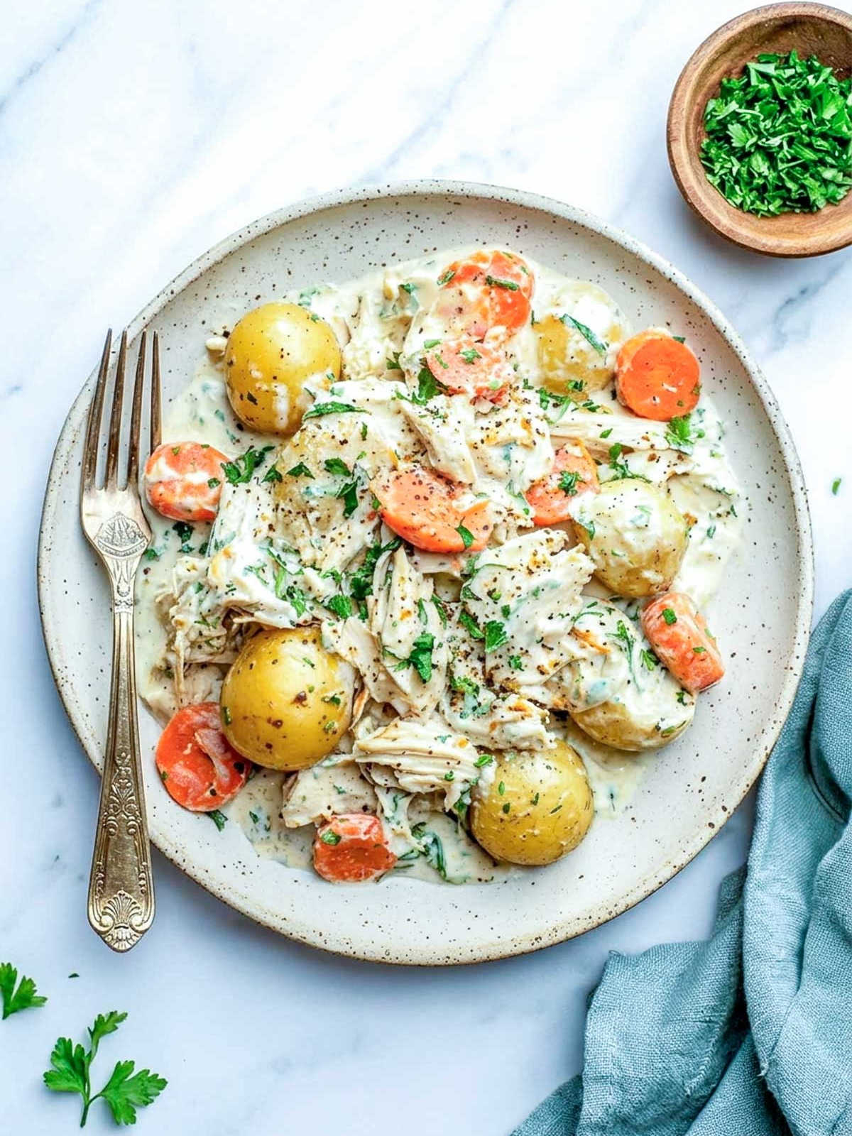 Top-down view of crockpot ranch chicken and vegetables with cottage cheese on a plate with parsley, black pepper, and a fork.