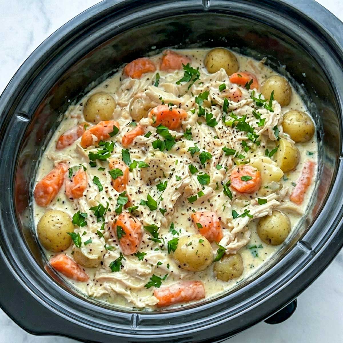 Finished crockpot ranch chicken and potatoes with carrots in a thick creamy ranch sauce, garnished with fresh parsley and black pepper directly in the slow cooker.