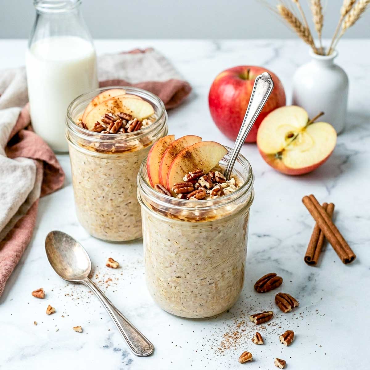 Apple pie kefir overnight oats in glass jars topped with sliced apples, pecans, and cinnamon.