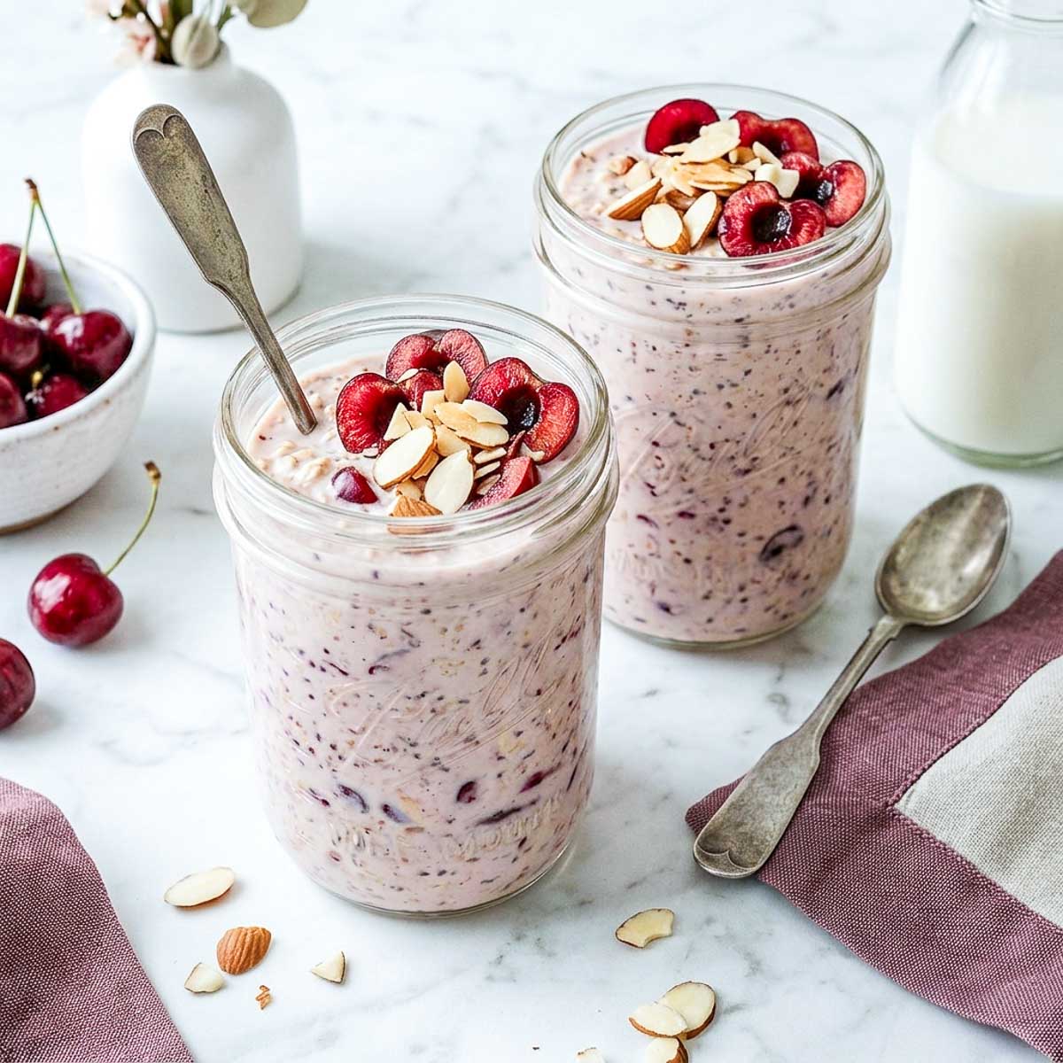 Cherry almond kefir overnight oats in glass jars topped with fresh cherries and sliced almonds.