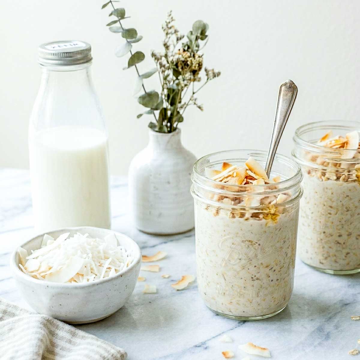 Coconut kefir overnight oats in glass jars topped with toasted coconut flakes.