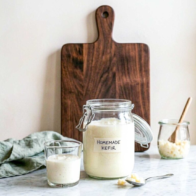 Homemade milk kefir in a labeled glass jar with a small glass of kefir and a jar of milk kefir grains beside it.