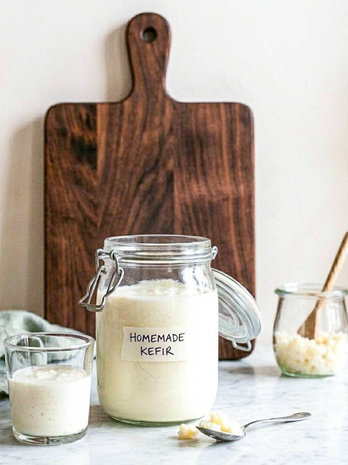 Jar of homemade milk kefir with a glass of fresh kefir and milk kefir grains on a spoon.