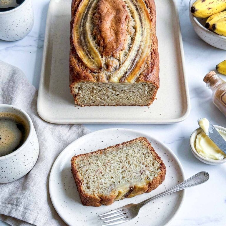 Overhead view of kefir banana bread with a slice on a speckled plate next to butter and coffee.