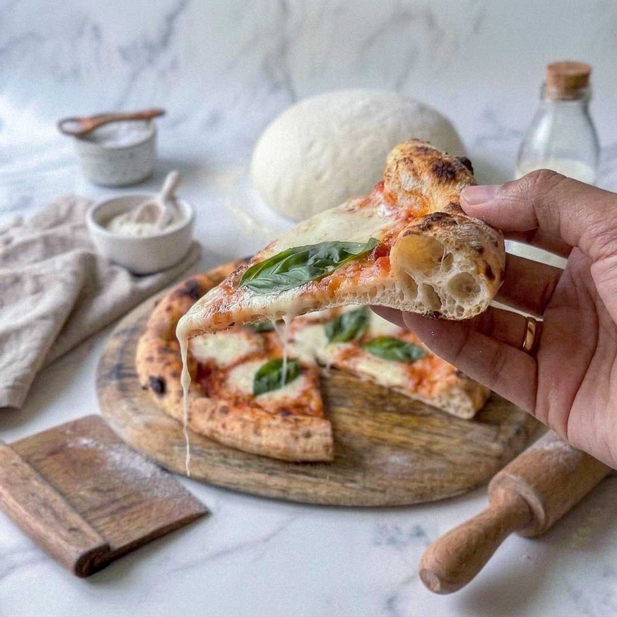 Slice of pizza made with kefir pizza dough held up to show an airy, chewy crumb.