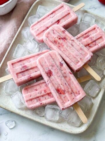 Strawberry kefir popsicles arranged on a tray of ice with fresh strawberries.