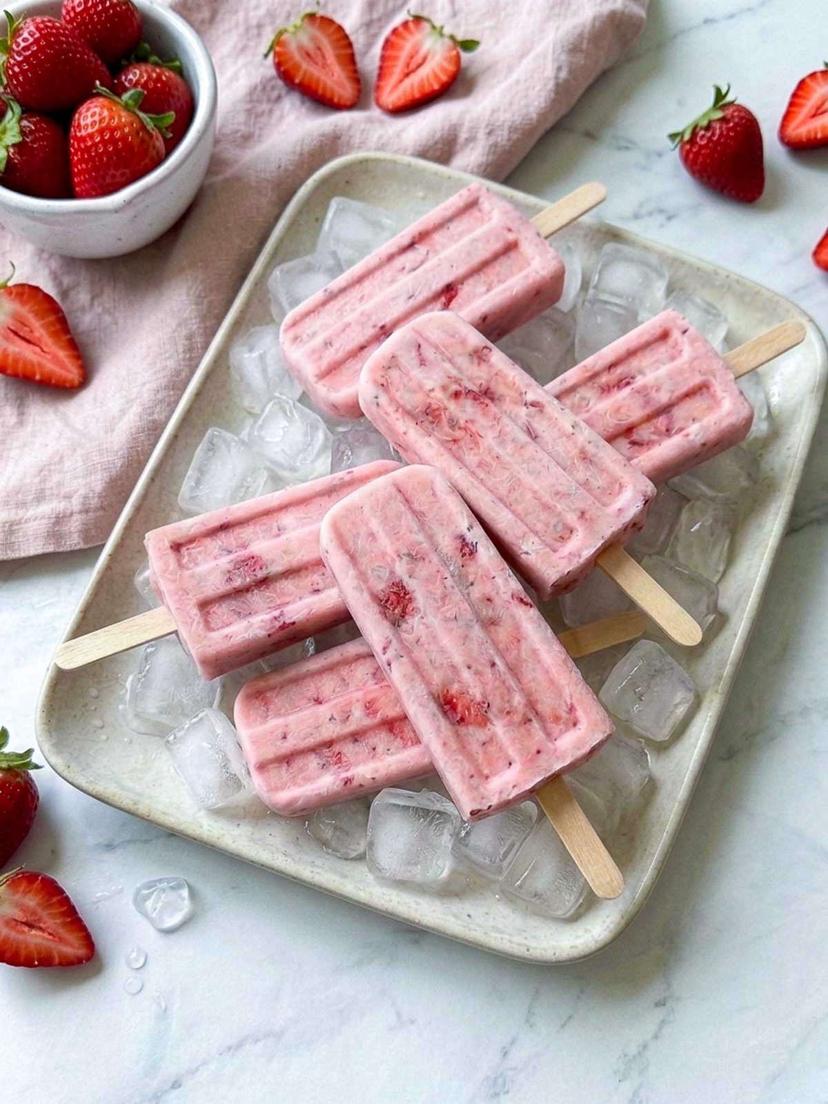 Creamy strawberry kefir popsicles with pieces of fresh strawberry, served on a tray of ice.