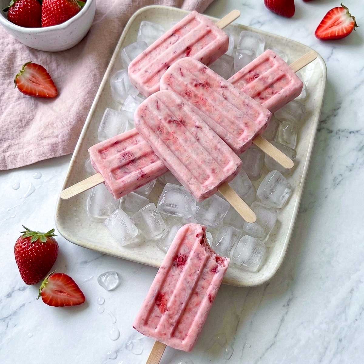 Strawberry kefir popsicles served over ice with one partially eaten popsicle in the foreground.