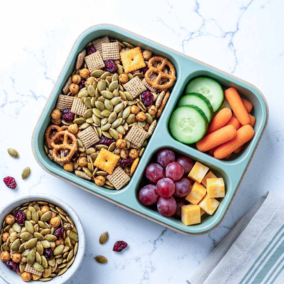 Nut-free pumpkin seed snack mix with roasted chickpeas, cereal, pretzels, crackers, and dried cranberries in a lunchbox.