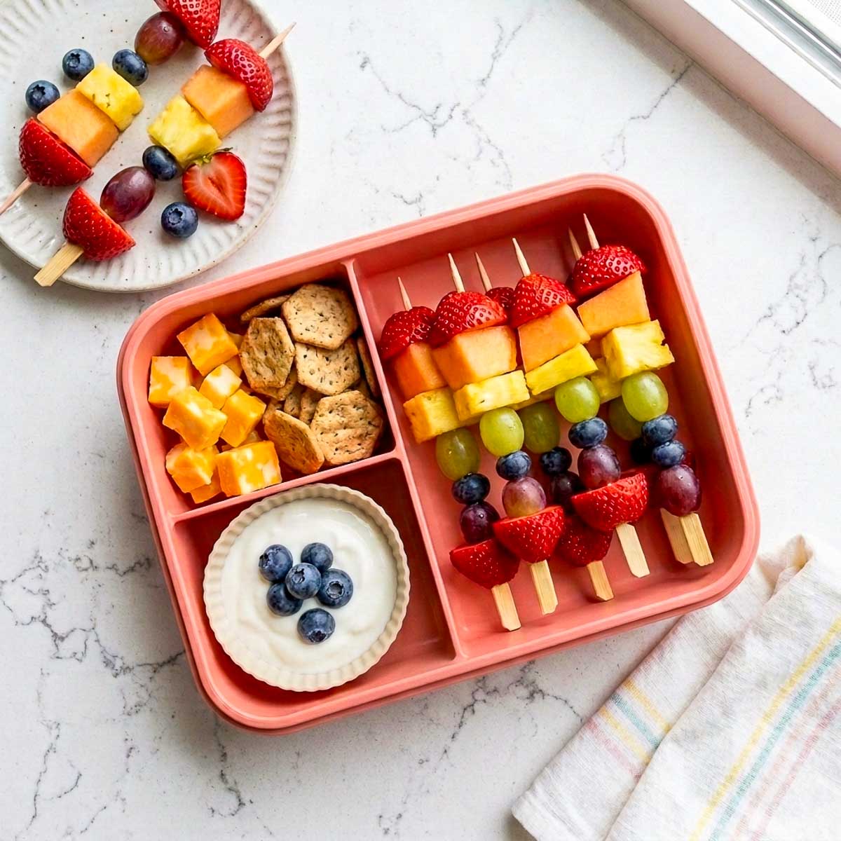 Rainbow fruit kabobs with strawberries, melon, pineapple, grapes, and blueberries packed with cheese, crackers, and yogurt dip.