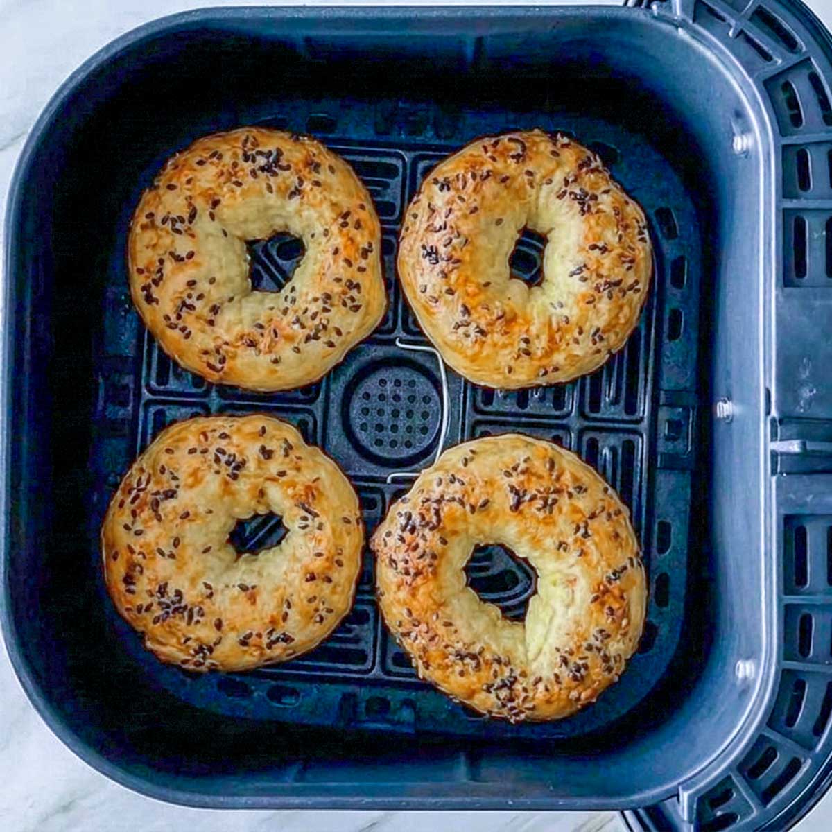 Four golden baked cottage cheese bagels in an air fryer basket after cooking.