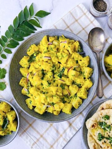 Curry potato salad in a gray bowl with curry leaves, red onion, and warm naan alongside.