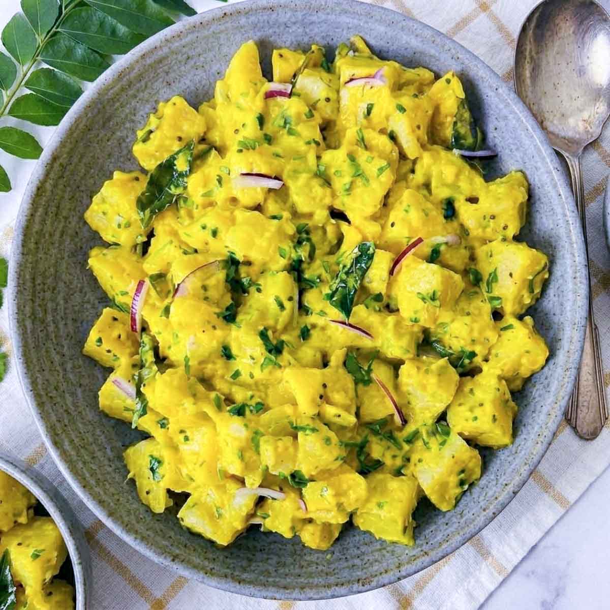 Top view of curry potato salad showing golden dressing clinging to potato cubes with cilantro and red onion.