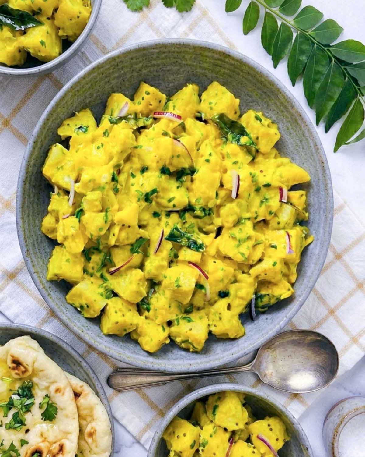 Close-up of curry potato salad showing golden dressing clinging to potato cubes with cilantro and red onion.