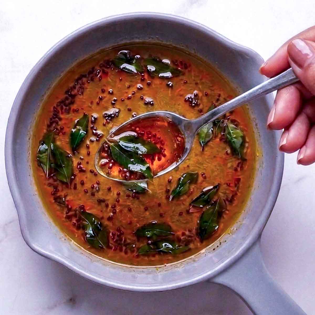 Curry powder, black mustard seeds, and curry leaves bloomed in hot oil in a small pan.