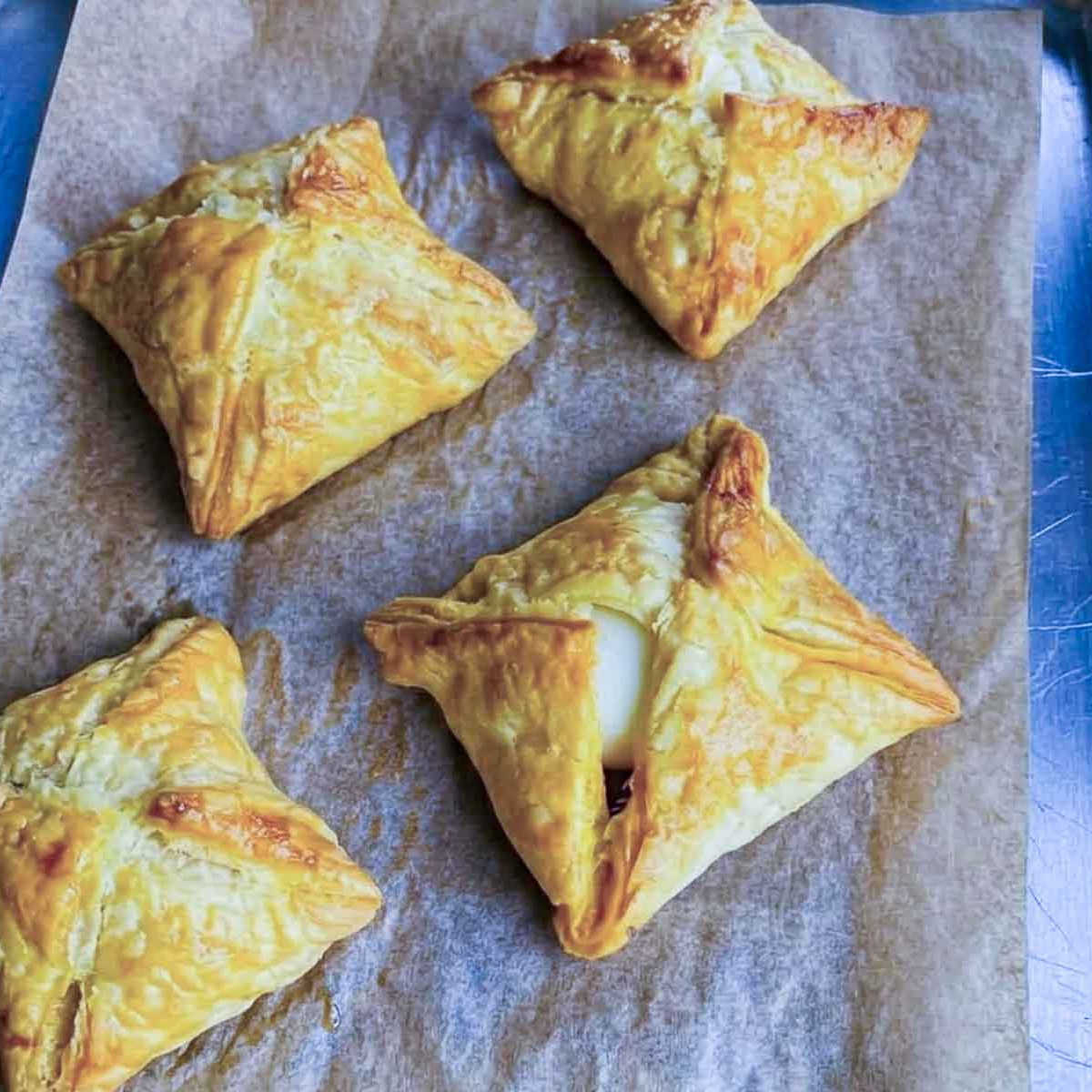 Baked egg puffs on parchment paper on a baking tray, golden with visible pastry layers.