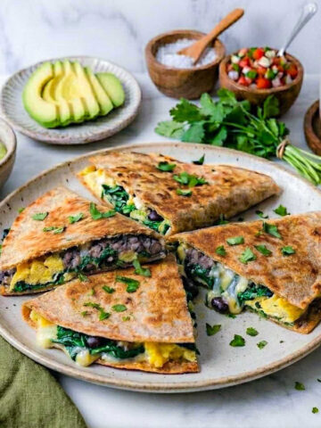 High-protein freezer breakfast quesadillas cut into wedges on a speckled plate with sliced avocado, pico de gallo, and coffee.
