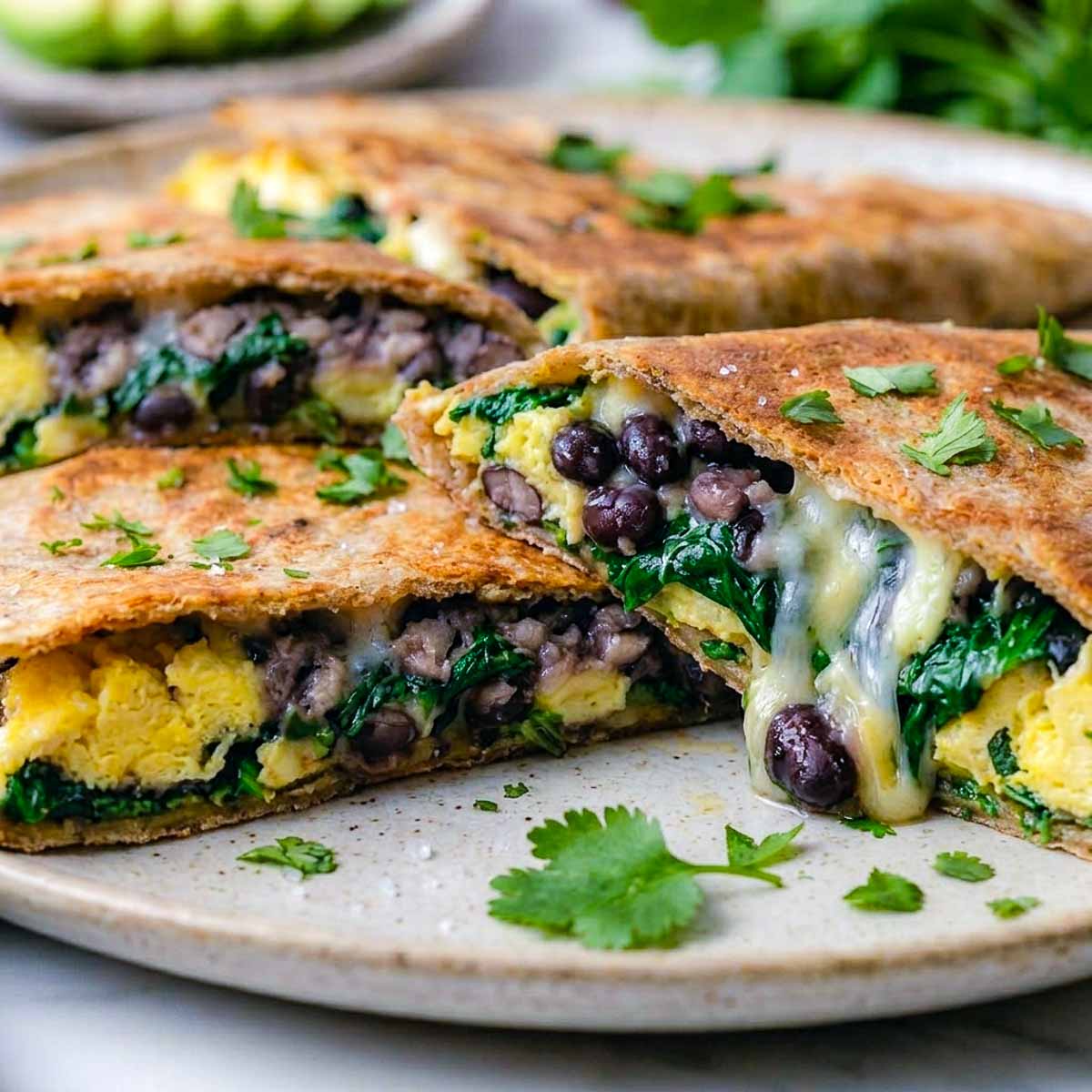 Close view of a black bean and egg freezer breakfast quesadilla wedge showing melted cheese, spinach, and scrambled egg.