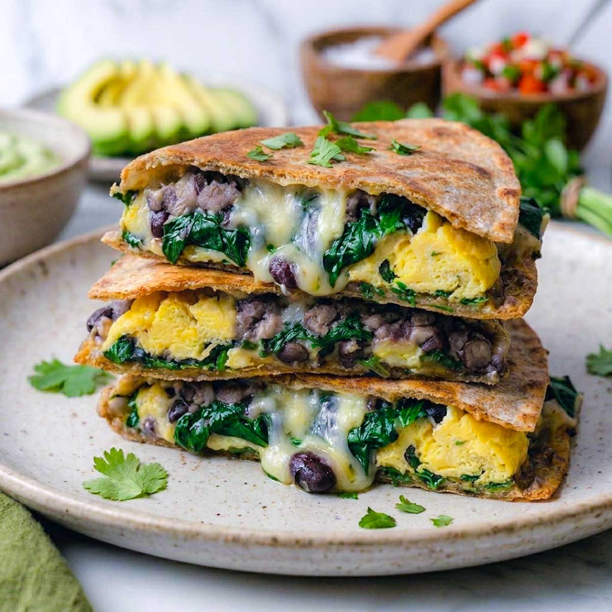 Stack of three high-protein freezer breakfast quesadilla wedges on a plate showing black beans, spinach, egg, and melted cheese.