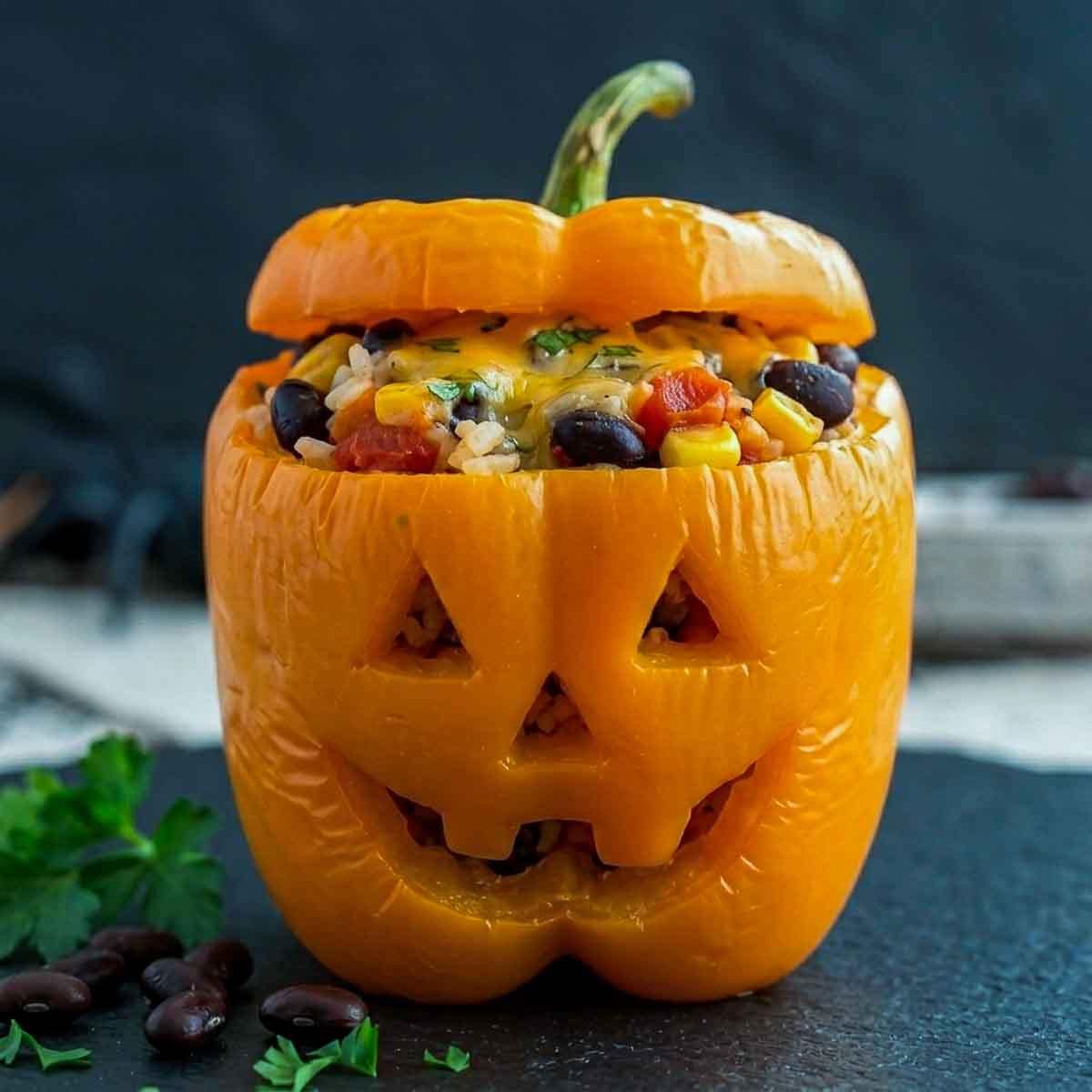 Close-up of a jack-o'-lantern stuffed pepper showing white rice, whole black beans, corn and diced tomato under melted cheese.
