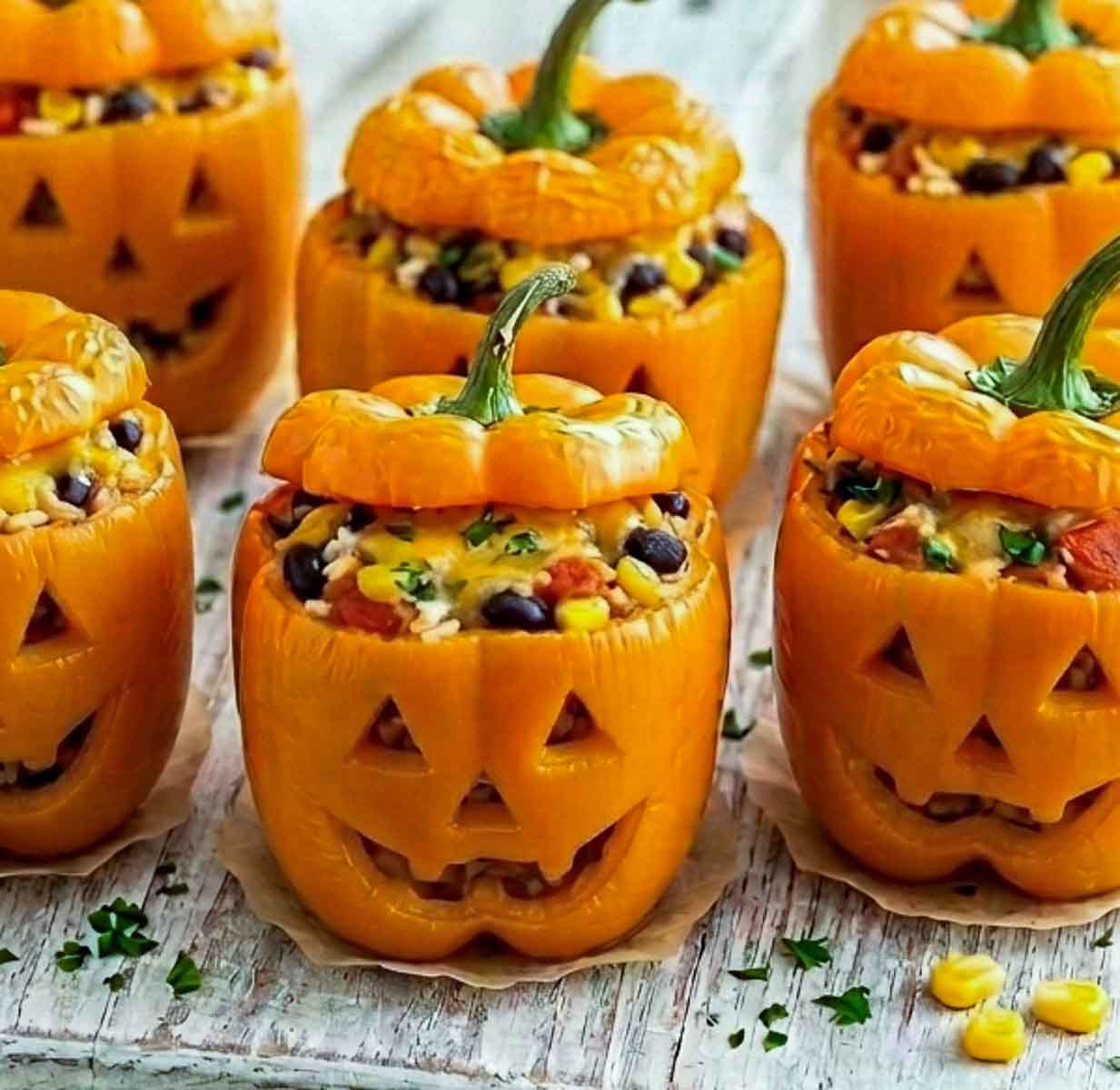 Close-up of six jack-o'-lantern stuffed peppers on a white rustic wooden board.